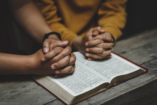 Christian couple or group of people holding hands praying worship together to believe and Bible on a wooden table for devotional for prayer meeting concept.