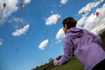 The boy in the purple dress flying a kite at the kite festival. A sunny spring day and a blue sky. The kite is flying and having fun.