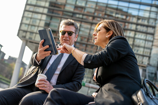 Two business people meeting outside and using a tablet, sunny light effect