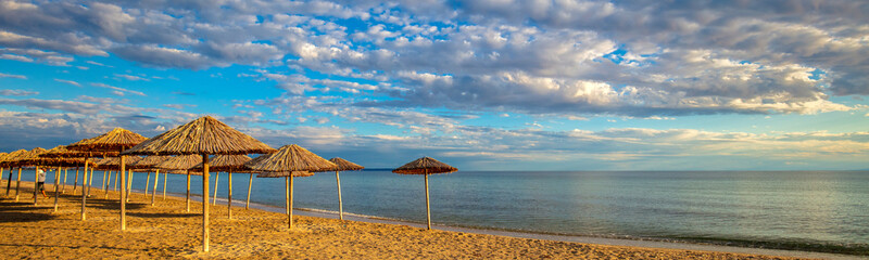 Seascape with straw umbrellas on a sandy beach. Beautiful cloudy sky. Horizontal banner