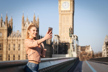 A London tourist woman stands alone in front of the Big Ben Tower and takes selfie photos with her...