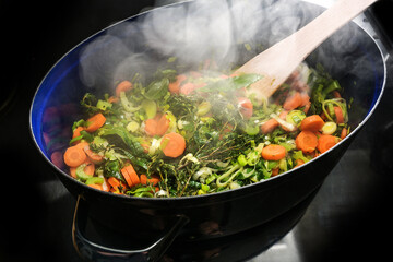 Steaming vegetables and herbs in a cooking pan on the black stove top, ingredients for a soup like...