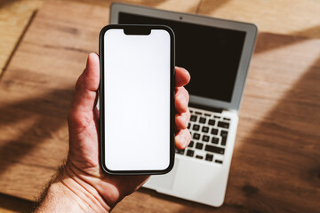 Smartphone mockup, man holding mobile phone with blank white screen over laptop computer