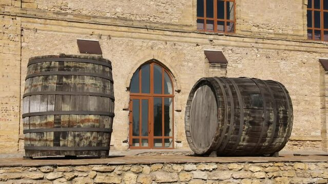 Large oak wine barrels outdoors on a sunny day near an ancient building. Ancient workshop with large display windows