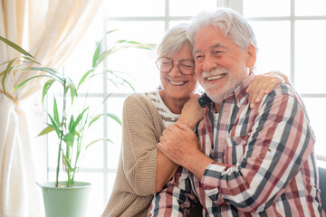 Happy senior couple embracing and laughing sitting at home. Modern retirees laugh at something funny, expressing happiness and carefree