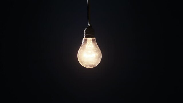 Incandescent lamp lights up and flickers on dark background. Classic bulb slowly turned on and off close-up. Warm flashing filament. Tungsten bulb cozy shine of vintage light. Idea, copy space 4K