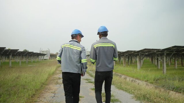 electrical engineer and  workman walking between solar panels on ecological field station,alternative energy,solar panel,controller box,green renewable energy,sustainability development energy concept