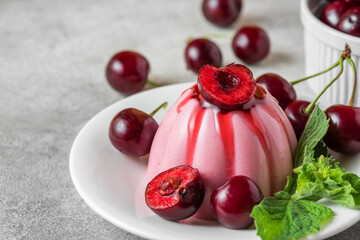 Delicious cherry panna cotta dessert with fresh cherry berries, fruit sauce and mint in a plate on gray table