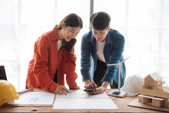 Young couple asian using laptop and looking into the blueprints of their new home. - Powered by Adobe