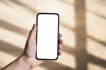 Hand holding white mobile phone with blank white screen in blur shadow background.
