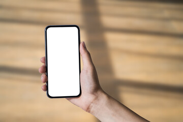 Hand holding white mobile phone with blank white screen in blur shadow background.
