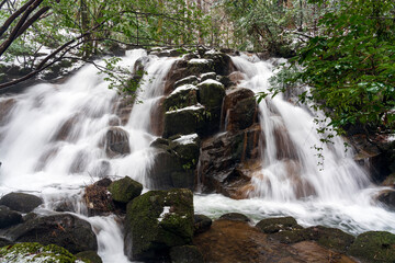 うっすらと雪化粧した森の中を流れる渓流と滝