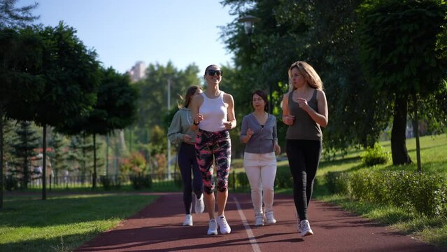 Wide shot group of positive fit sportswomen jogging in slow motion. outdoors. Dolly shot portrait of beautiful confident Caucasian women talking smiling running in sunny park