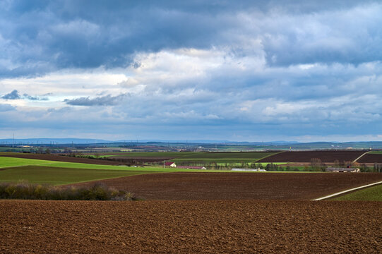 Winterliches Feld ohne Ansaat mit wolkenverhangenem Himmel bei Schweinfurt, Franken, Deutschland