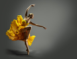 Ballerina in Yellow Chiffon Dress dancing over Gray Background. Ballet Dancer jumping in Air in...