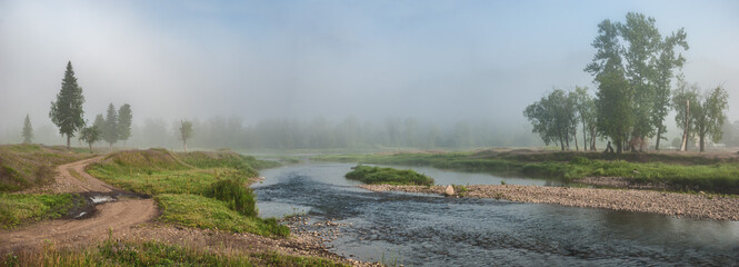 trees near the mountain river. Panorama of the morning view of the mystical forest in the fog, mountain landscape