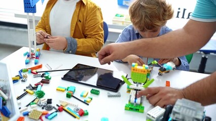 Robotics programming class. Children construct and code Robot. STEM education using constructor blocks and laptop tablet, remote control joystick. Technology educational development for school kids