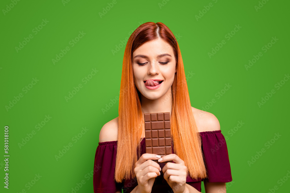 Sticker Young red-haired girl holding a chocolate bar isolated on yellow background