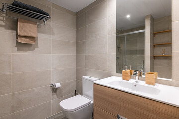 Empty bathroom with toilet and sink with large cabinet with gray tiles and big mirror with towels....