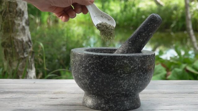 The hand is putting fresh spices into the grey stone mortar 