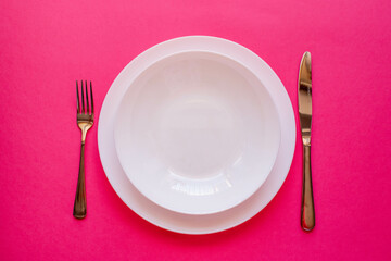  The concept of gastronomy and food. Top view of an empty white plate with fork and knife against a pink background. Serving dinner in a restaurant.