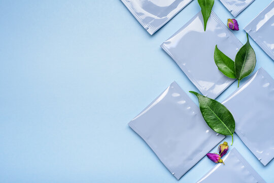 Blue plastic tea bag sachets or envelopes with dry rosebuds and green leaves.