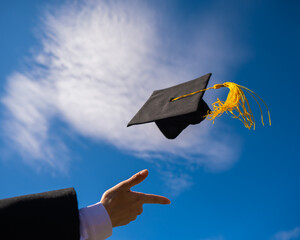 Close-up of a woman's hand with a graduation cap against the blue sky. 