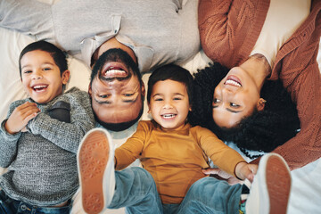 Happy, above and portrait of a family on a bed for relaxation, bonding and quality time. Laughing, smile and carefree parents with children in the bedroom to relax and play in the morning together