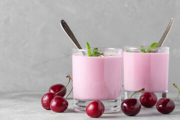 Two glasses of healthy cherry yogurt with fresh berries, oats, spoon and mint on gray background. Healthy breakfast