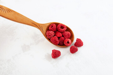 Freeze dried raspberries in wooden spoon on light textured surface. Selective focus, copy space....