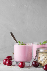 Cherry berry yogurt in glasses with fresh berries, oatmeal, mint for healthy breakfast on gray background. Vertical orientation