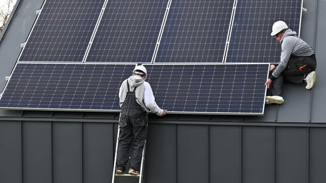 Technicians building photovoltaic solar module station on roof of house. Men electricians in helmets installing solar panel system outdoors. Concept of alternative and renewable energy.
