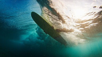 Surfer underwater. Young man in the ocean. Surfer paddles the surfboard to pass the wave in the...