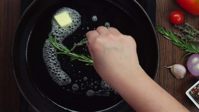 Top view hand putting a sprig of thyme on a hot frying pan 