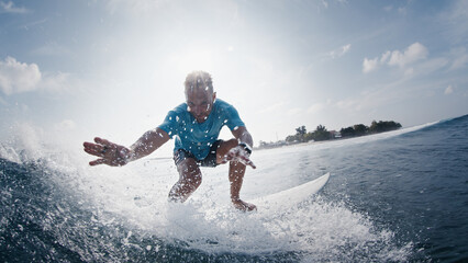 Surfer rides the wave. Young man surfs the ocean wave in the Maldives and looks into the camera