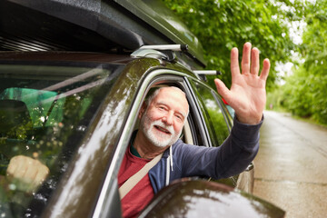 Happy elderly man waving hand while driving car