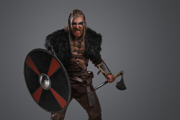 Shot of angry scandinavian barbarian dressed in leather armor against grey background.
