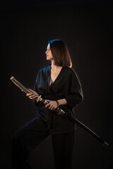 Fototapeta premium Young beautiful woman in black kimono with japanese sword on black background.