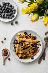 Crepes or blinis or thin pancakes with blueberries, hazelnuts and chocolate sauce on a white plate...