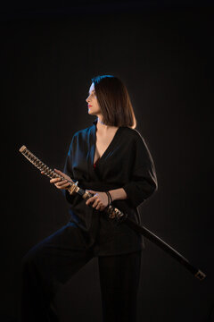 Young beautiful woman in black kimono with japanese sword on black background.