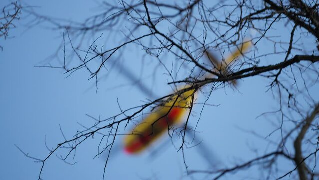 Tracking shot of a defocused ADAC german rescue helicopter flying over trees in a blue sky on rescue mission