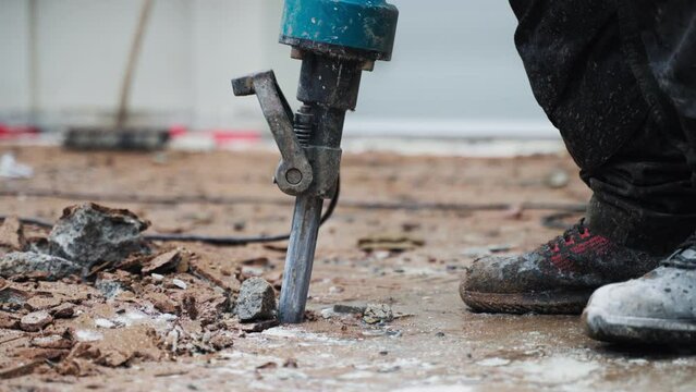 Man worker with jackhammer machine destroying asphalt or concrete road - close-up - reveal shot