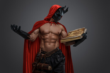 Portrait of evil fanatic with red cloak and mask against grey background.