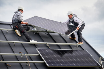 Technicians installing solar panel system on roof of house. Men workers in helmets carrying...