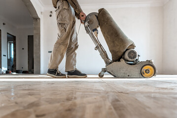 Professional carpenter grinding a wooden parquet floor by using floor sander in newly constructed...