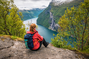 Woman with backpack sitting on the rock over Geiranger fjord - obrazy, fototapety, plakaty