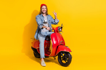 Fototapeta na wymiar Full length photo of funky cool man wear denim jacket riding moped showing v-sign isolated yellow color background