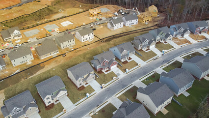 Suburban subdivision with two story houses under construction, building envelope near completed homes with lush tree in Flowery Branch, Georgia, USA