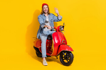 Fototapeta na wymiar Full length photo of cool friendly man wear denim jacket waving arms palm riding moped isolated yellow color background