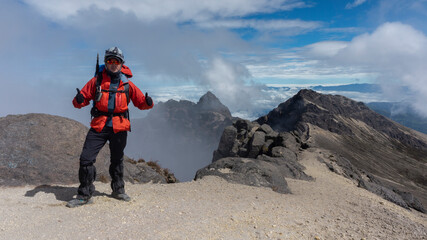 Young man climber standing on the summit of Guagua Pichincha volcano wearing red coat and helmet